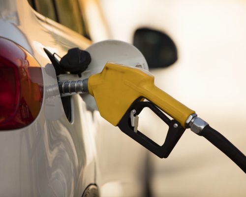 A white car at a gas station being filled with fuel